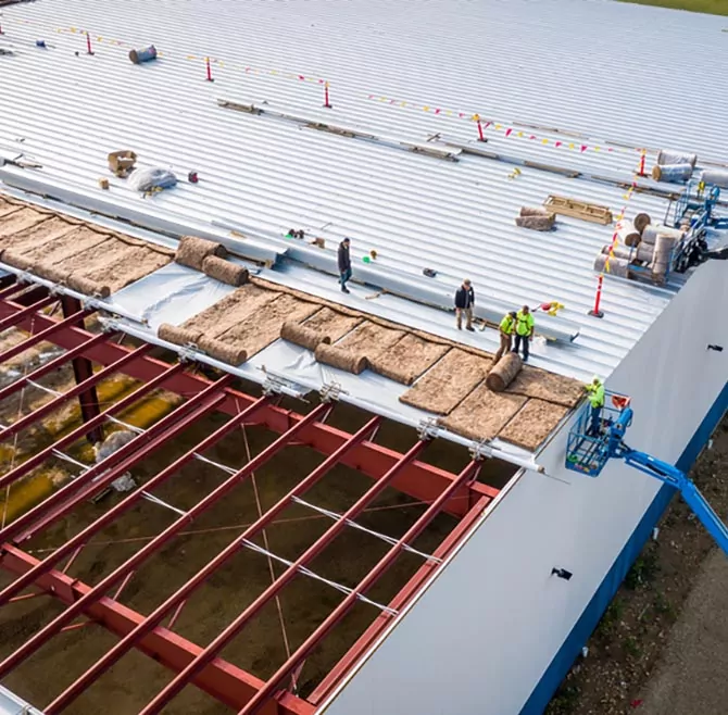 MILWAUKEE, WI, USA - SEPTEMBER 15, 2020: Construction workers installing insulation and roof panels on a large warehouse building.